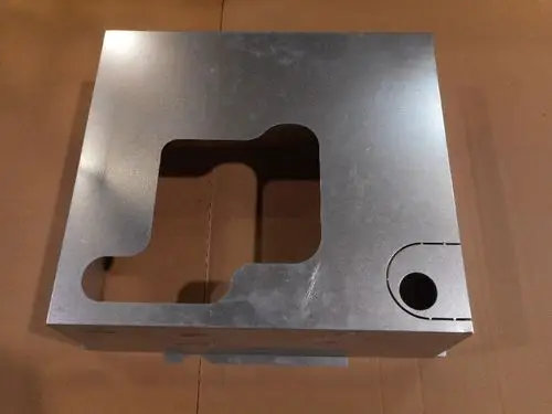 Metallische Hinterwand von Remeha mit einer Öffnung und einer runden Aussparung, auf einer braunen Box liegend.